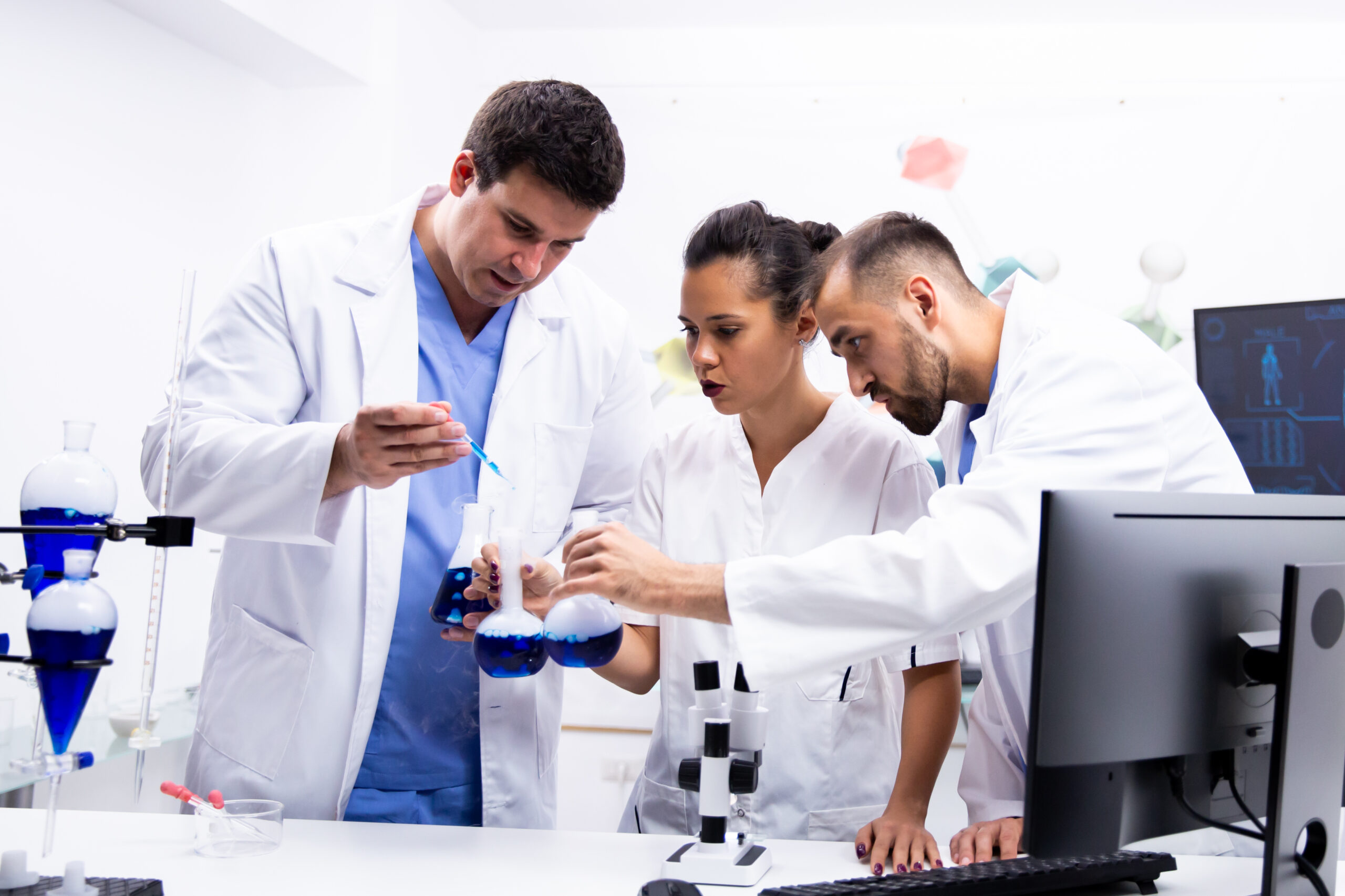 Team of scientist in white coat working together with smoking blue liquid in modern research lab.